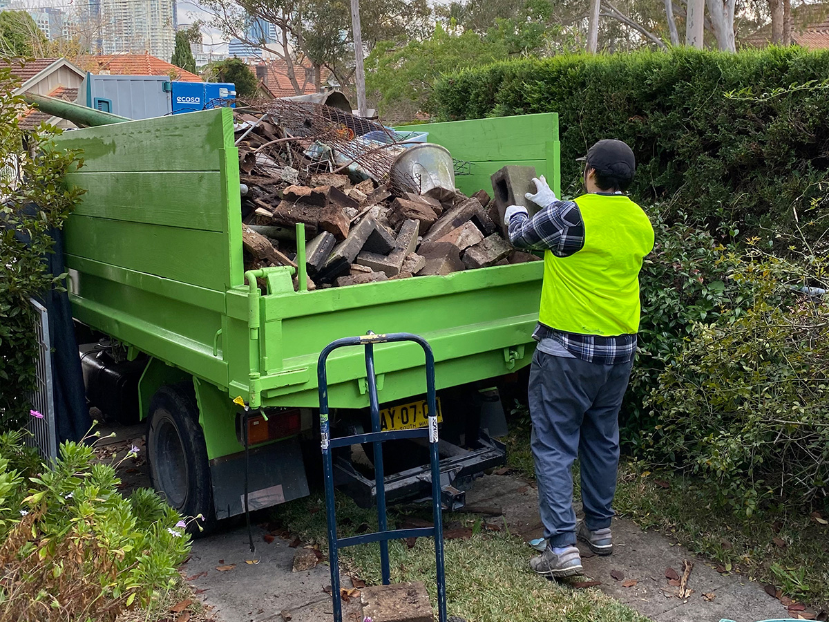 Rubbish removal truck being loaded by team member.