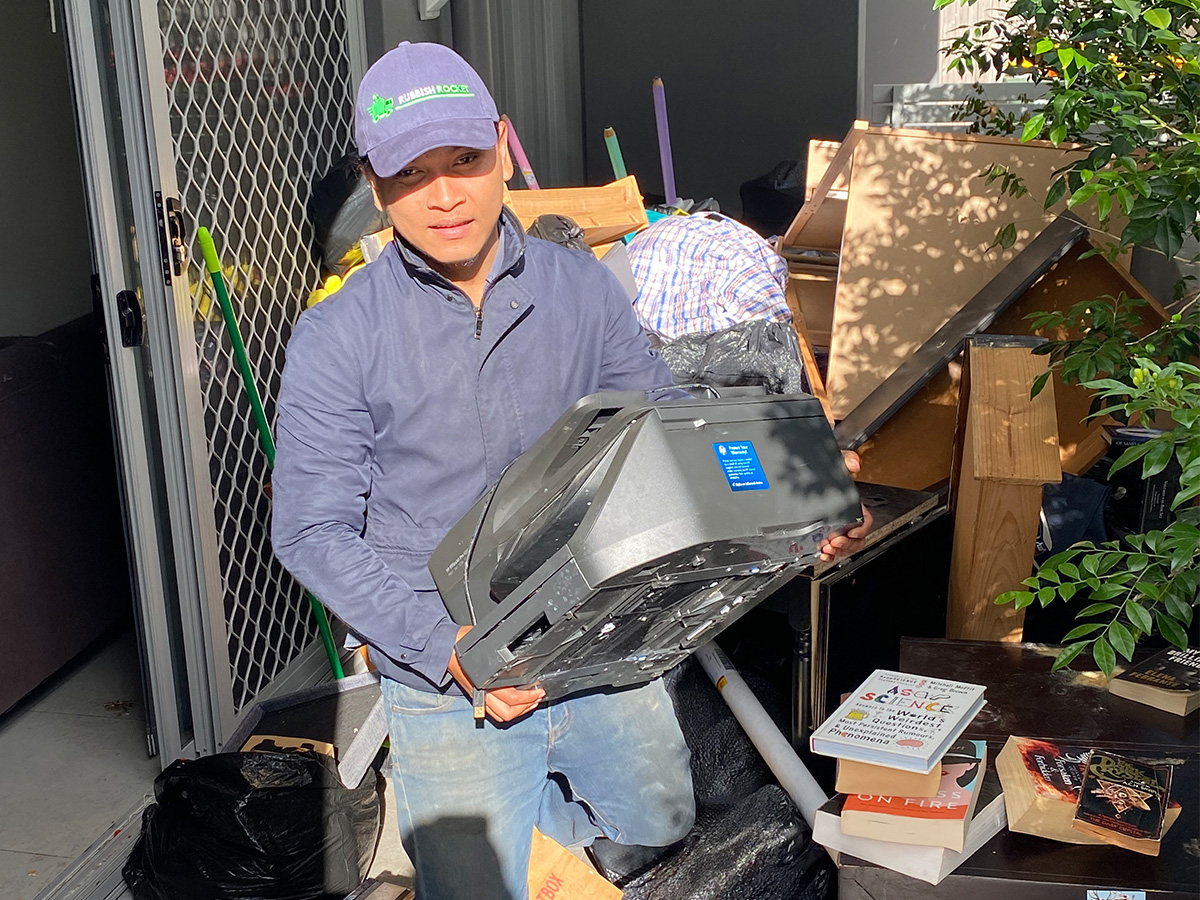 Team member with printer in hands and rubbish behind sorting waste showcasing eco-friendly service.